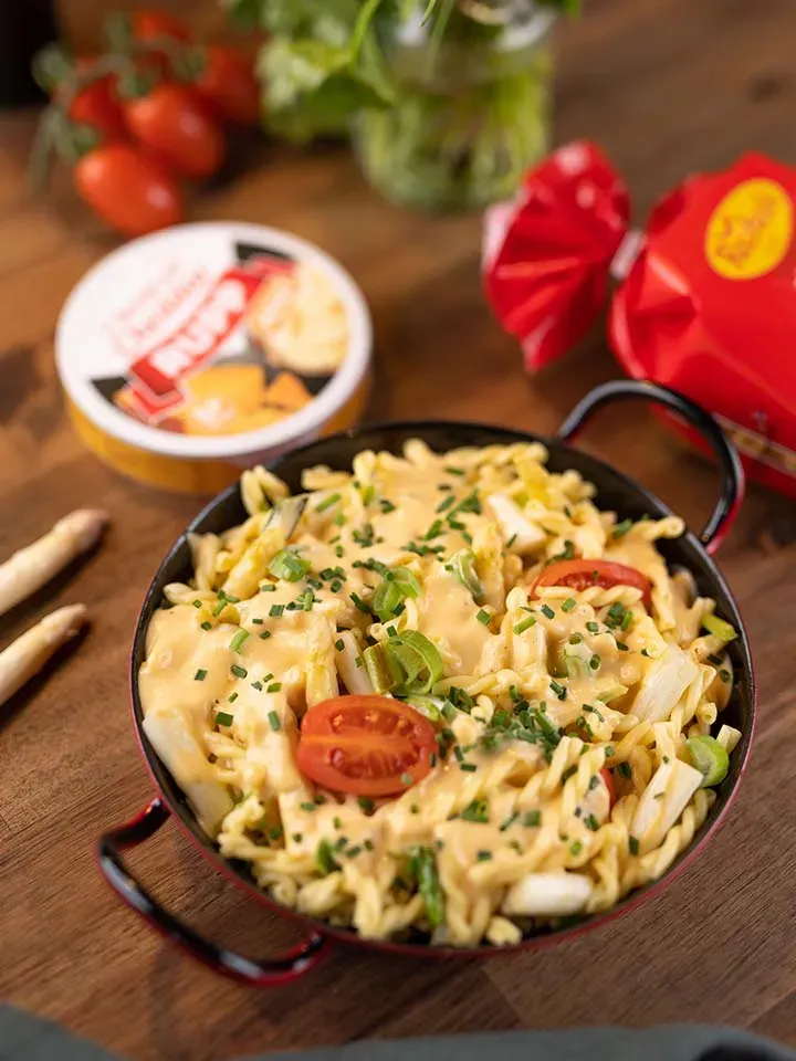 Nudelpfanne mit Käsesauce, Tomaten und Kräutern auf Holztisch