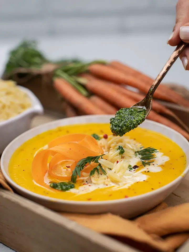 Löffel gibt grünes Pesto auf Karottencremesuppe mit Nudeln und Karottenscheiben