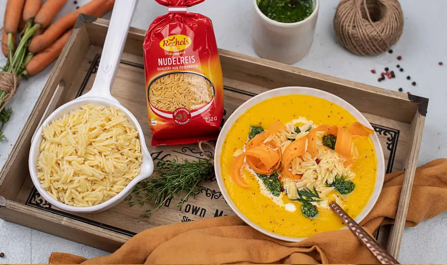 Karottencremesuppe mit Nudeln und frischen Karotten auf einem Holztablett