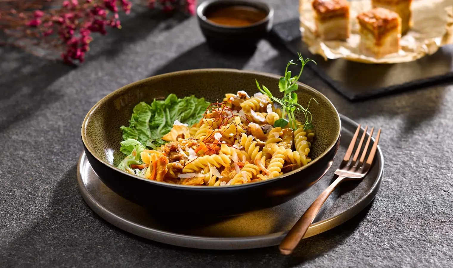 Kimchi-Carbonara mit Spiralnudeln, Salat und Kräutern auf dunklem Untergrund mit Gabel