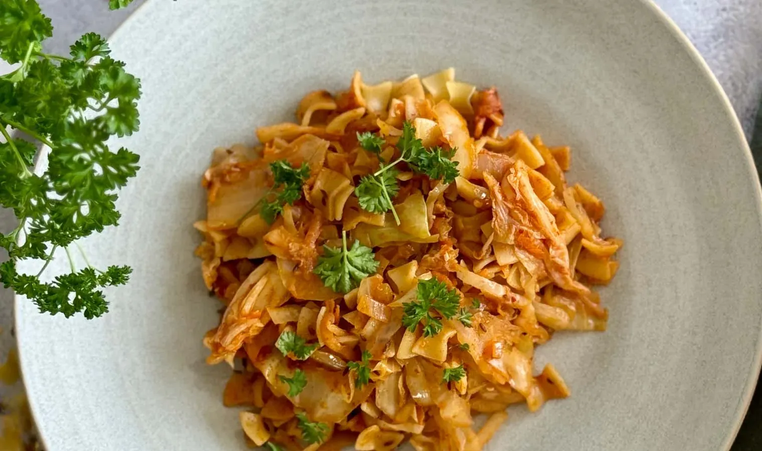 Kimchi-Fleckerlspeis mit gebratenem Kohl und Petersilie auf einem Teller