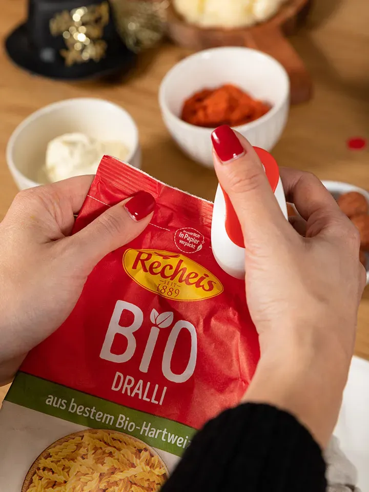Hände öffnen eine Packung Recheis Bio Dralli mit einem roten Clip