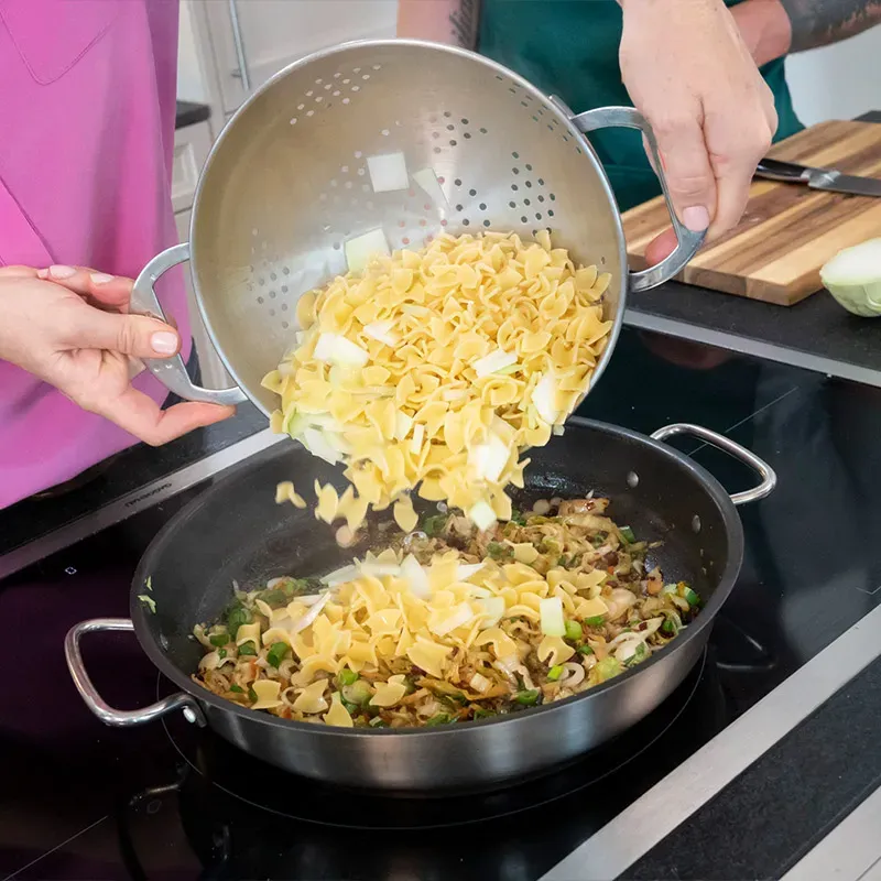 Krautfleckerl Next Generation: Fleckerl und Zwiebeln werden aus dem Sieb in eine Pfanne mit Gemüse gegeben