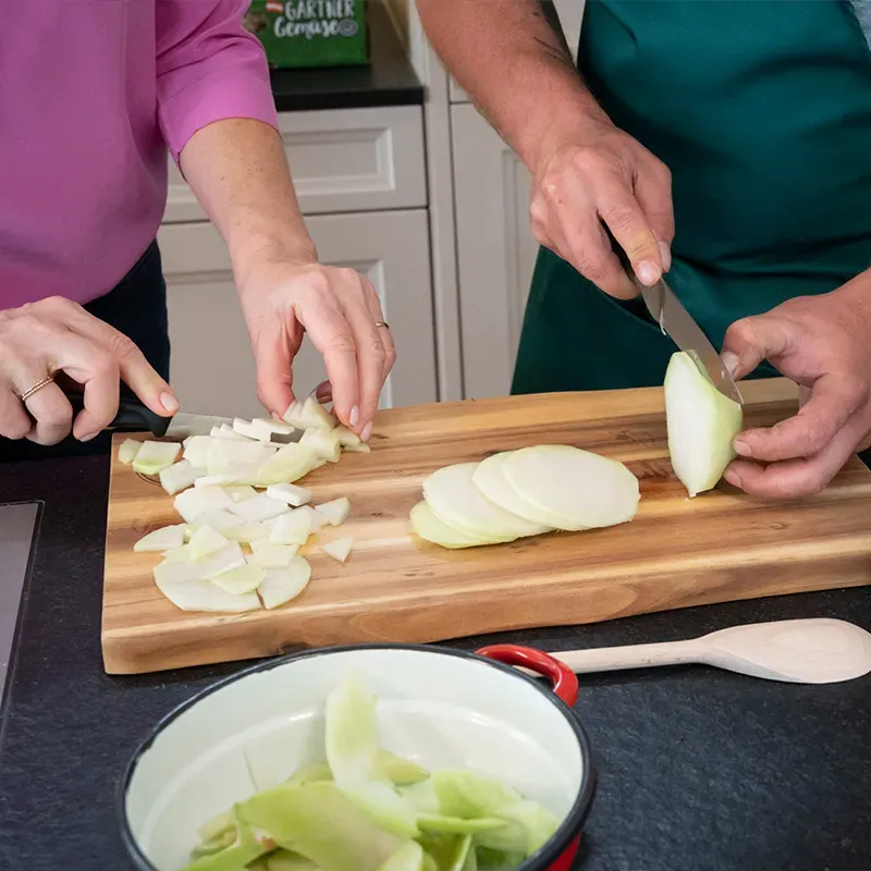 Krautfleckerl Next Generation: zwei Personen schneiden Fleckerl-Gemüse und Kohlrabi auf einem Holzbrett in der Küche