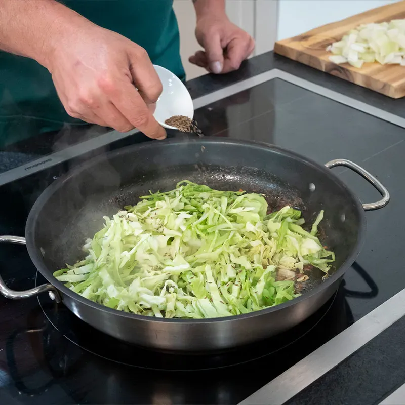 Krautfleckerl Next Generation: Person gibt Gewürze in eine Pfanne mit angebratenem Weißkraut