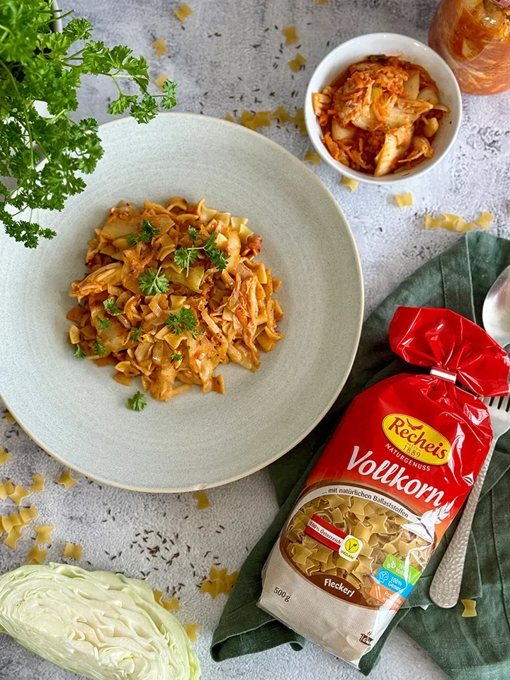 Veganes Krautfleckerl aus Vollkornnudeln mit Kraut und Petersilie neben Nudeltüte und Kraut