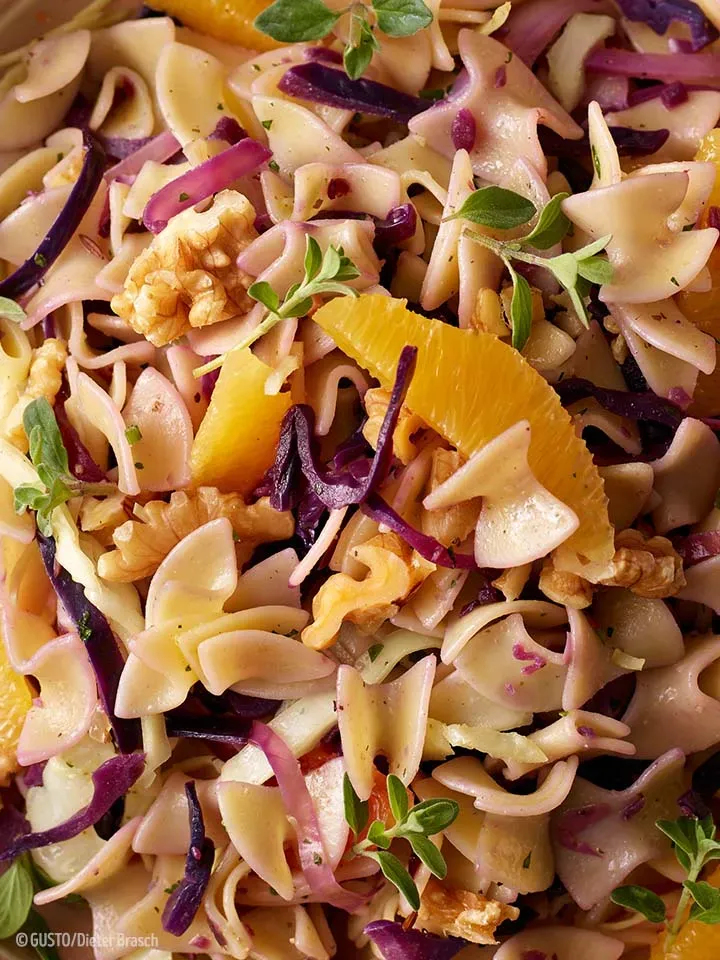 Nahaufnahme von rotweißem Krautfleckerl-Salat mit Nudeln, Walnüssen, Orangenscheiben und frischen Kräutern