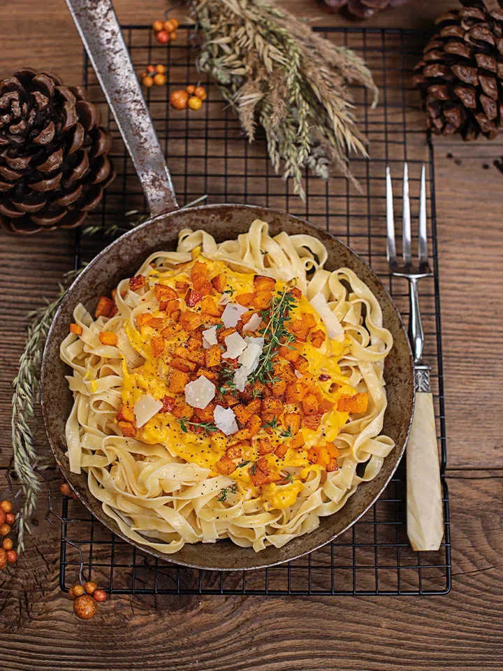 Kürbis-Carbonara mit Bandnudeln in der Pfanne, mit Kräutern und Parmesan dekoriert