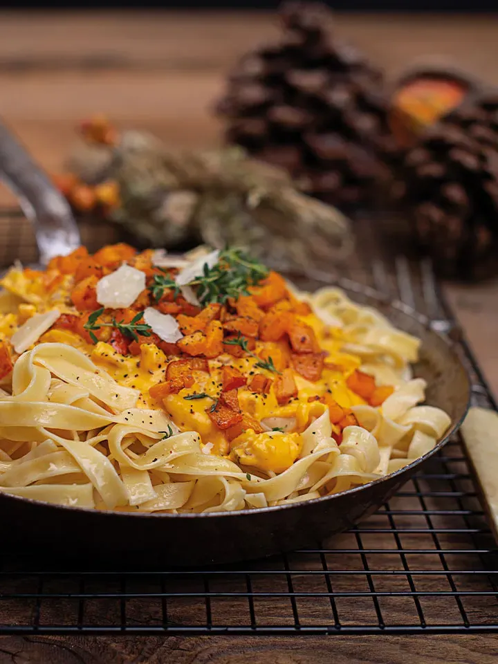 Kürbis-Carbonara: Nudeln mit Kürbisstücken und Kräutern in einer Pfanne auf einem Gitter