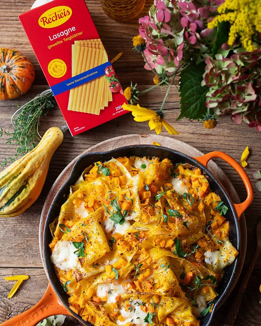Kürbislasagne mit Käse als One-Pot in der Pfanne, daneben Lasagnepackung, auf Holztisch