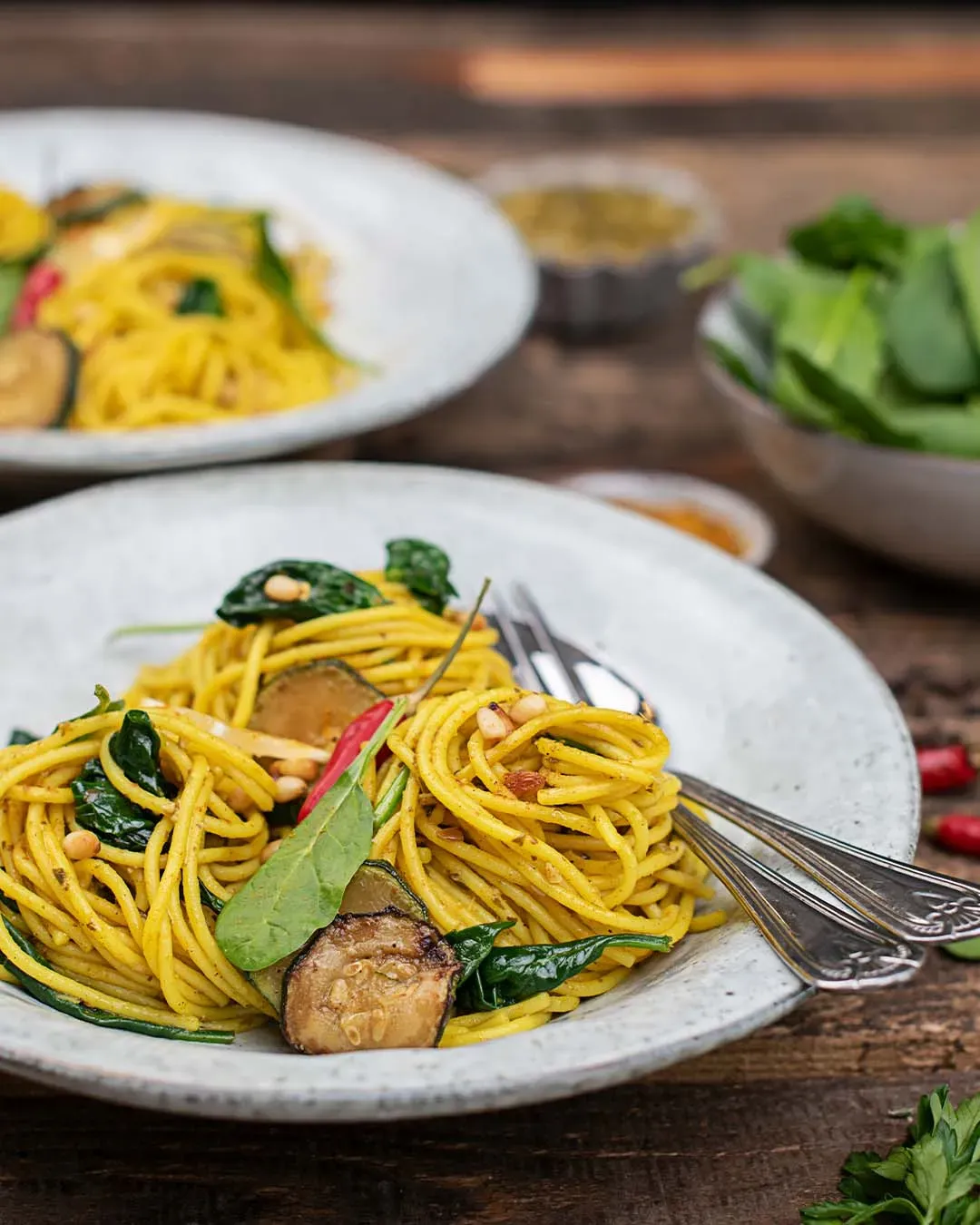 Kurkuma-Spaghetti mit Zucchini, Spinat und Pinienkernen auf einem Teller auf Holztisch