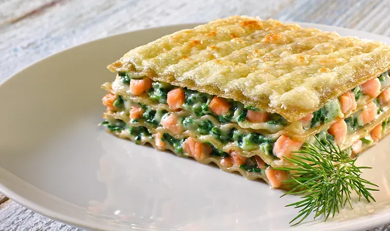 Mehrschichtige Lachs-Lasagne mit Spinat auf weißem Teller