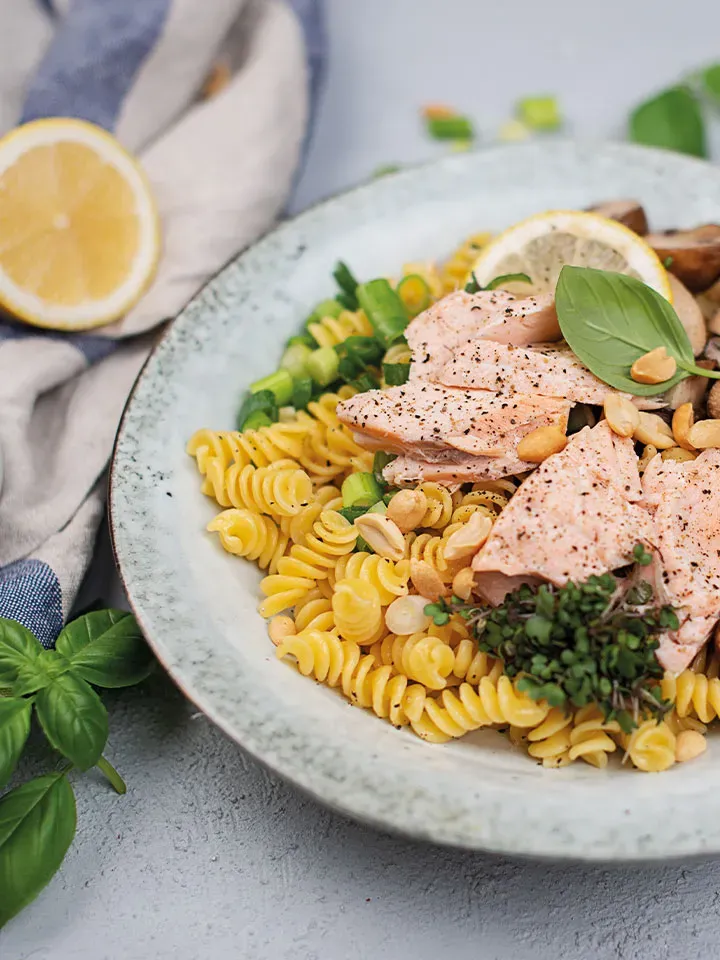 Lachs-Nudel-Bowl mit Erdnüssen und frischen Kräutern auf einem Teller