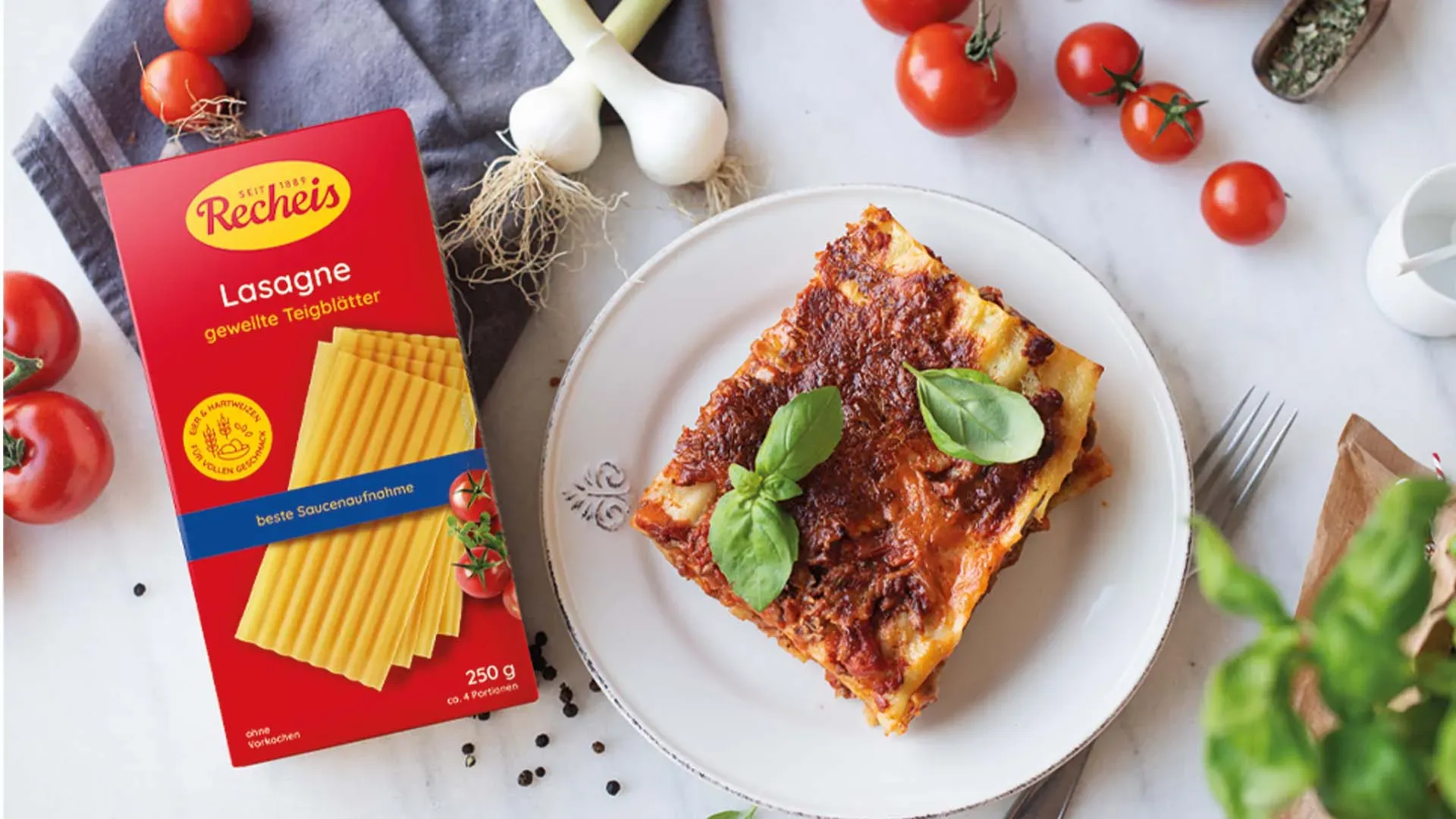 Lasagne al forno auf Teller mit Lasagneblättern, frischen Tomaten und Knoblauch
