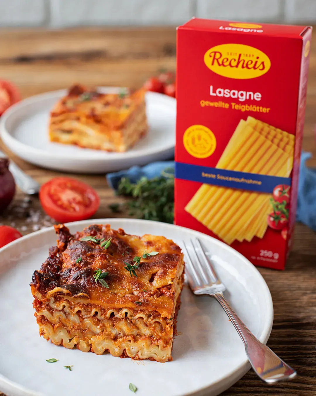 Ein Stück Lasagne mit Fleisch auf einem Teller vor einer Packung Lasagne-Nudeln