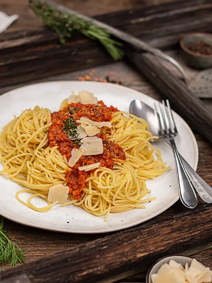 Vegane Linsenbolognese mit Spaghetti, Tomatensauce und Parmesan auf einem Teller auf rustikalem Holztisch