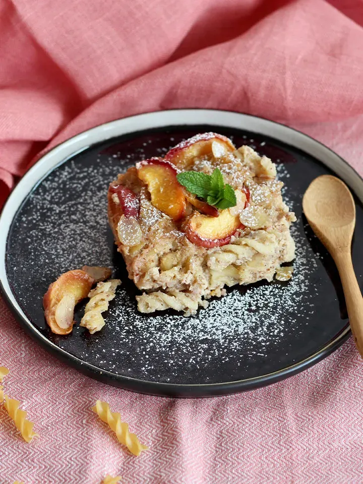 Low-Carb-Auflauf mit Pfirsich und Puderzucker auf schwarzem Teller