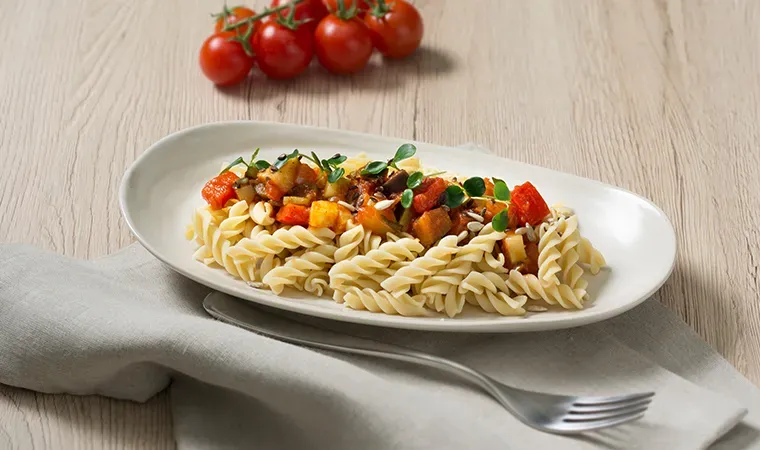 Low-Carb-Dralli mit Gemüseragout und Powerkernen: Spiralnudeln mit Gemüse auf Tuch mit Gabel und Tomaten
