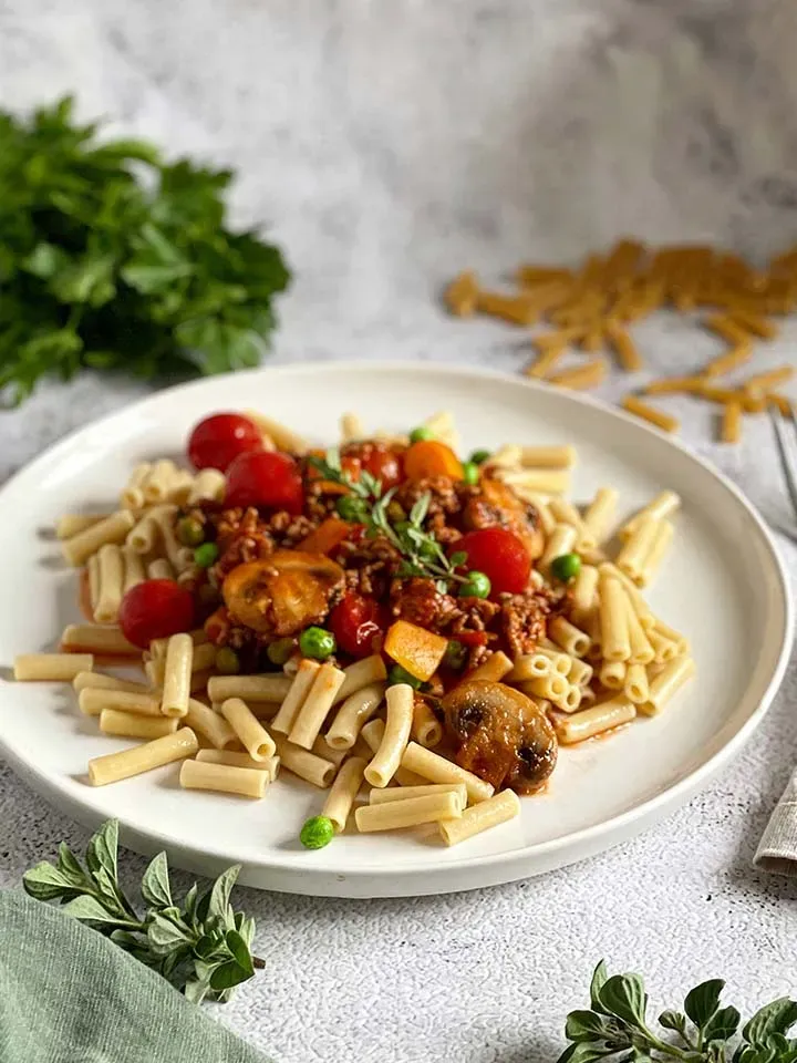 Low-Carb-Hirtenmakkaroni mit Tomatensauce, Pilzen, Erbsen und Kirschtomaten auf einem Teller