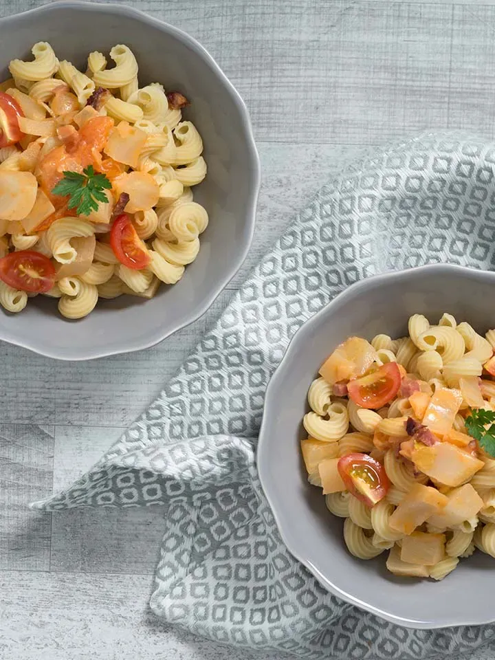 Low-Carb-Hörnchen mit Fenchel und Tofu, Spiralnudeln mit Tomaten und Kräutern in zwei Schalen auf grauem Tuch