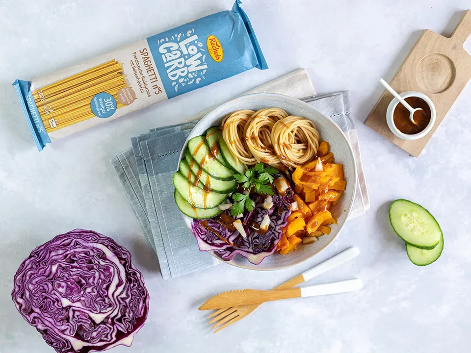 Low-Carb-Nudelbowl mit Spaghetti und frischem Gemüse neben Rotkohl und Gurkenscheiben