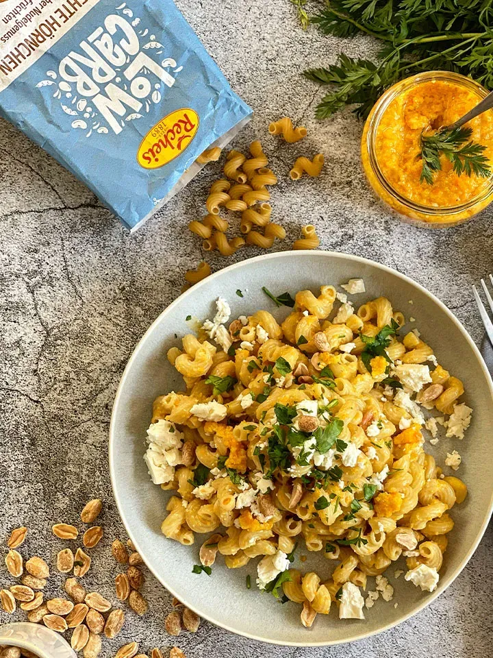 Low-Carb-Nudeln mit Käse, Kräutern und Erdnüssen auf einem Teller auf Steinuntergrund