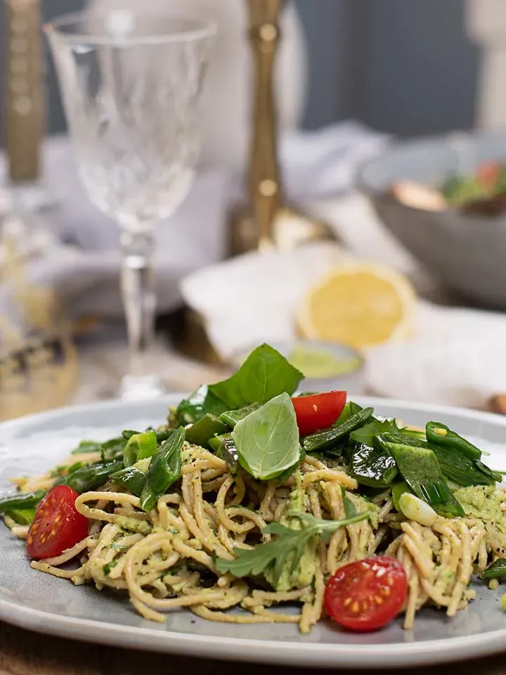 Low-Carb-Spaghetti mit Avocadopesto, grünen Blättern und Kirschtomaten auf einem Teller auf gedecktem Tisch