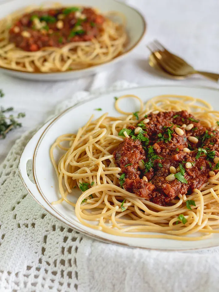 Vegane Low-Carb-Spaghetti Bolognese mit Kräutern und Pinienkernen auf einem Teller