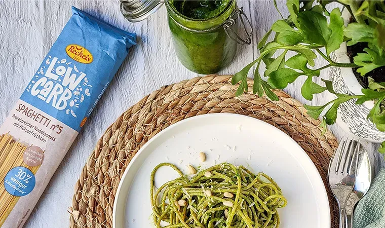 Low-Carb-Spaghetti mit Bärlauchpesto auf einem Teller neben Kräutern und Besteck