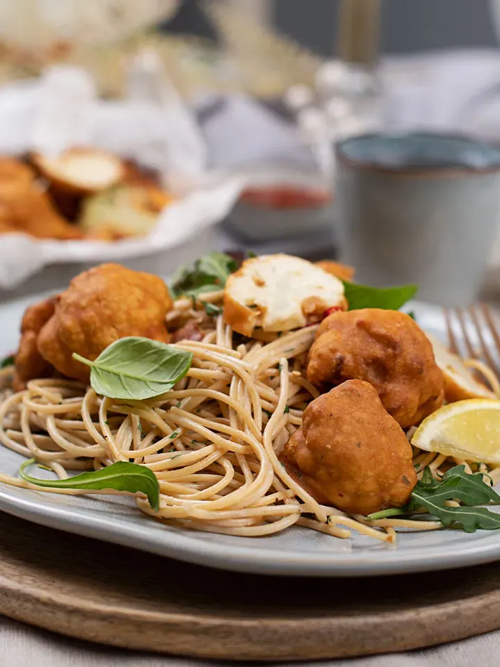 Low-Carb-Spaghetti mit Blumenkohl, frittierten Bällchen, Salat und Zitronenscheibe auf einem Teller
