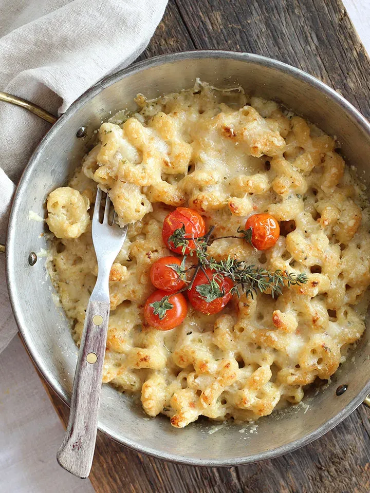 Low-Carb-Mac-and-Cheese: überbackene Pasta mit Tomaten und Kräutern in der Pfanne auf Holzuntergrund