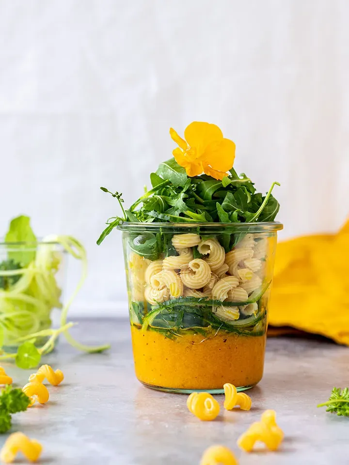 Low-Carb-Mealprep-Nudelsalat im Glas, geschichtet, mit einer gelben Blüte obenauf