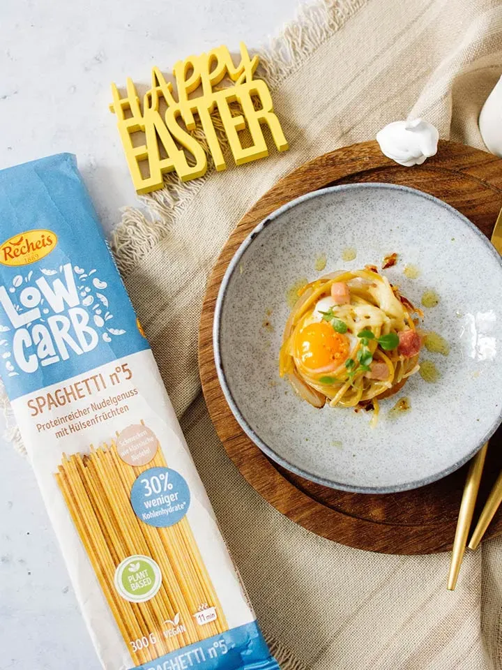 Low-Carb-Spaghetti-Muffins mit Ei auf einem Teller, daneben Low-Carb-Spaghettipackung und Happy-Easter-Deko