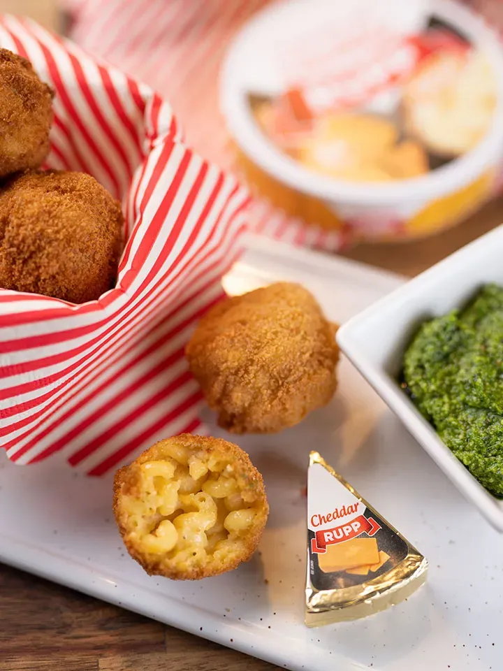 Frittierte Mac-and-Cheese-Nudelbällchen als Snack mit Käse und grünem Dip auf weißem Teller