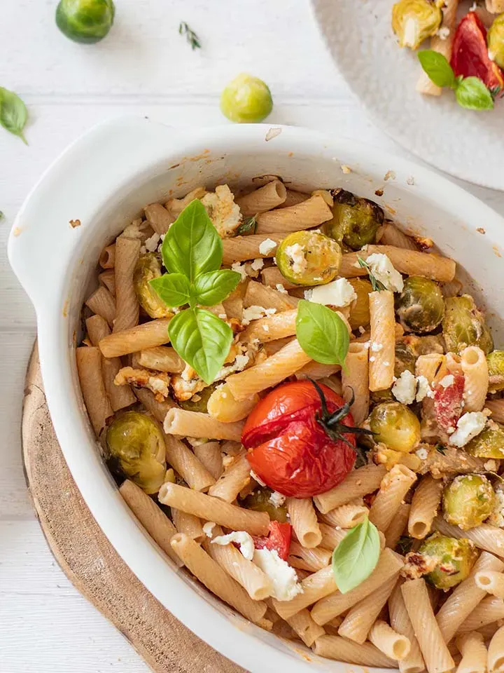 Makkaroni-Nudelauflauf mit Kohlsprossen, Feta, Tomate und Basilikum in weißer Auflaufform