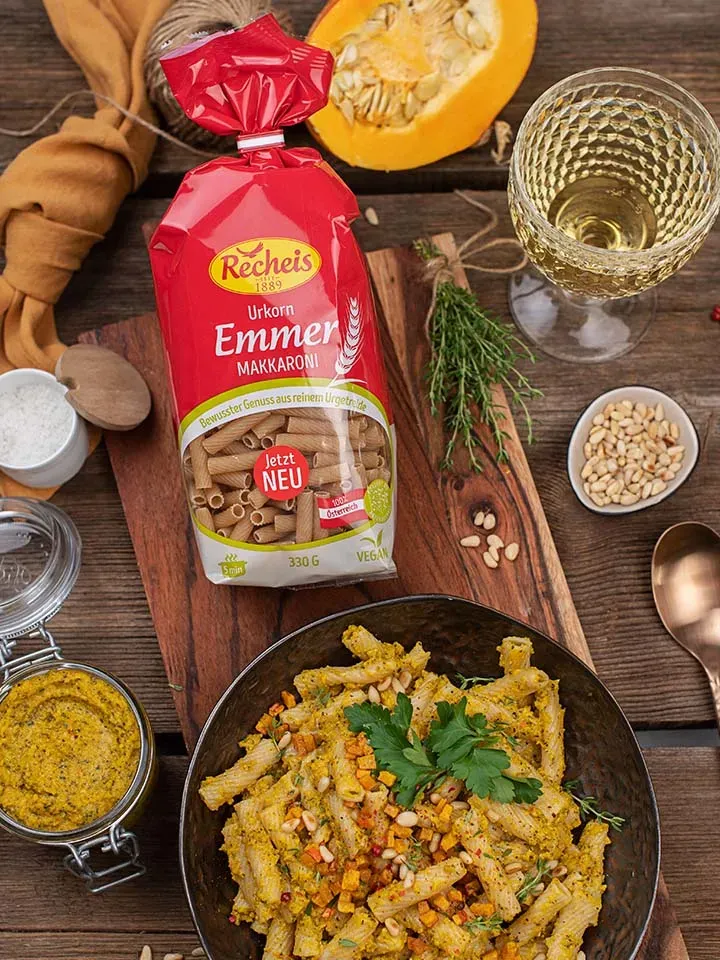 Makkaroni mit Kürbispesto: Emmer-Makkaroni mit Kürbis und Kräutern, dazu ein Glas Weißwein, auf Holztisch