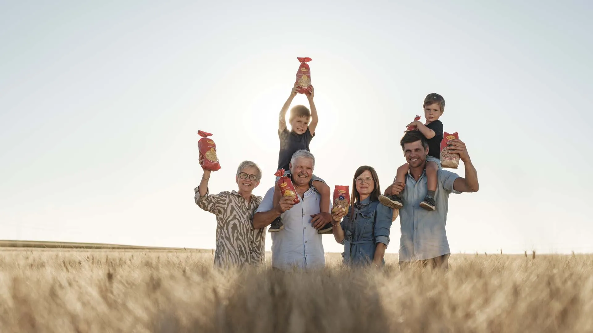 Mehrgenerationenfamilie hält Getreideprodukte in einem Weizenfeld bei Sonnenuntergang