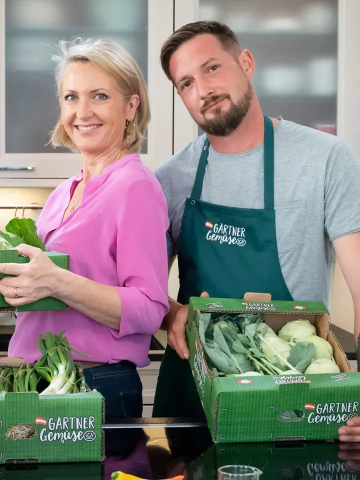 Martina Hohenlohe und Florian Mössinger halten Kisten mit frischem LGV-Gärtnergemüse in einer Küche