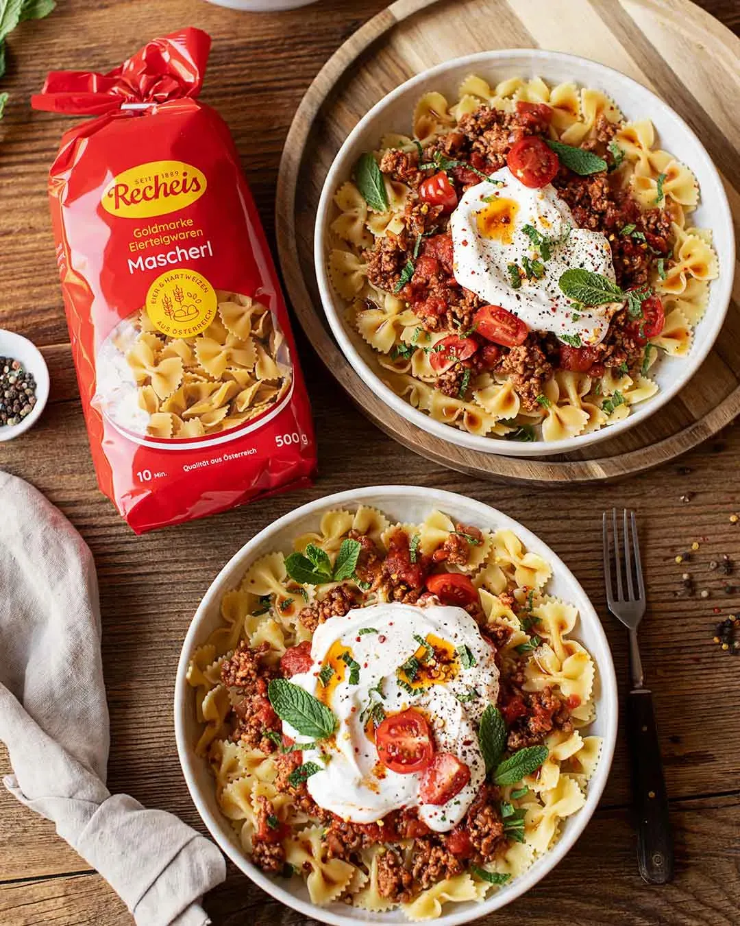Türkische Nudeln mit Mascherl, Hackfleischsoße, Tomaten und einem Klecks Joghurt auf zwei Tellern