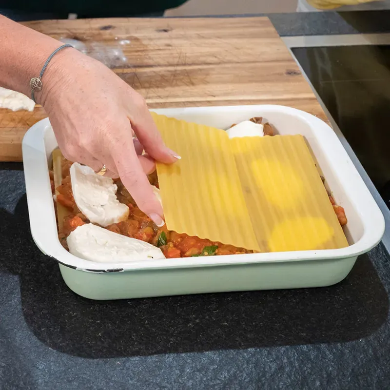 Melanzani-Lasagne: Hand legt Lasagneblätter in Auflaufform mit Tomatensoße und Käse