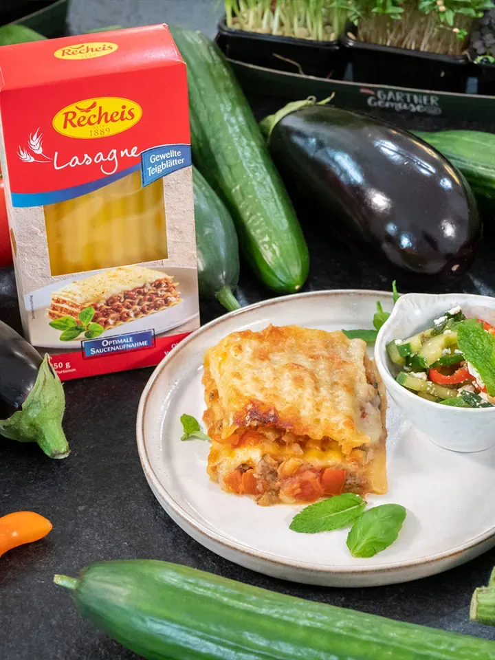 Melanzani-Lasagne von Martina Hohenlohe auf Teller mit Gemüse, im Hintergrund Packung Lasagne-Nudeln