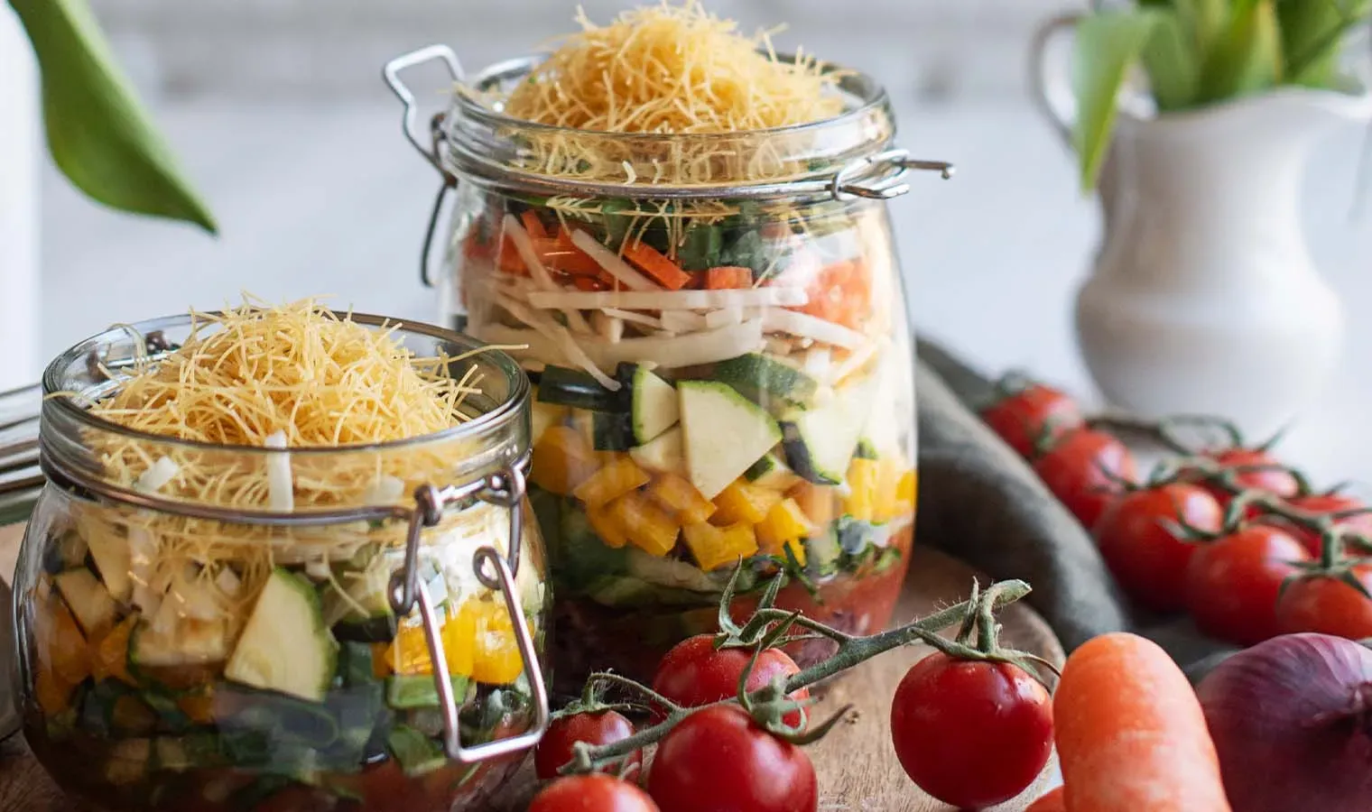 Minestrone aus dem Glas: zwei Einmachgläser mit geschichteten Gemüsestücken, davor Tomaten