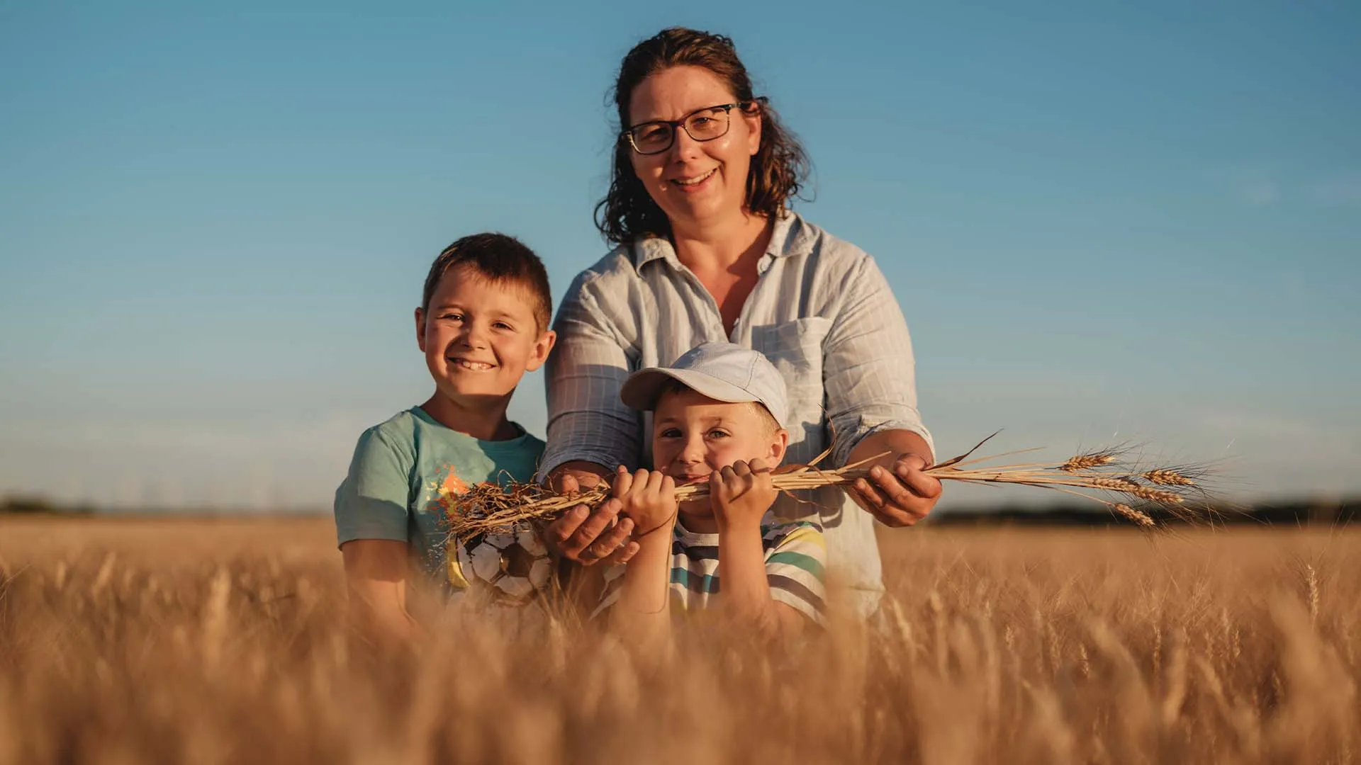 Frau mit zwei Kindern hält Getreide in einem Feld bei Sonnenuntergang