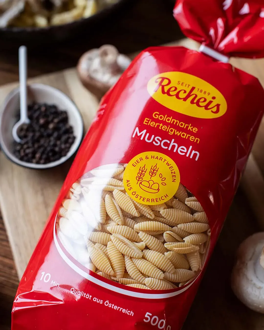 Packung Recheis Muschelnudeln mit Pilzgulasch, Gewürzen und Pilzen auf einem Holzbrett