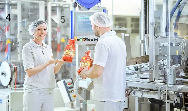 Zwei Mitarbeiter in Schutzkleidung prüfen verpackte Nudeln in einer Produktionsanlage, Thema nachhaltige Verpackung