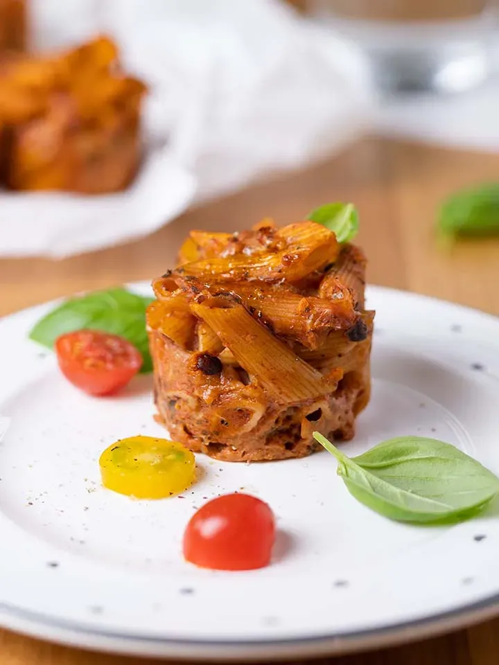 Nudelmuffin aus gebackenen Penne mit Tomatensauce und Basilikum auf weißem Teller