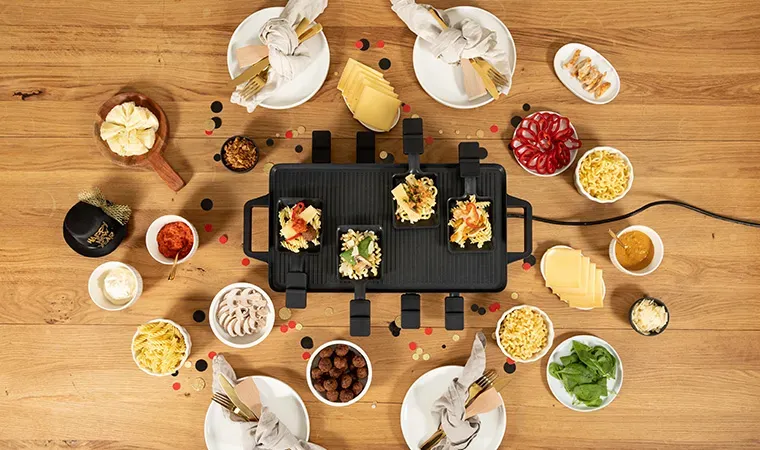 Nudelraclette-Ideen: Tisch mit Raclette-Grill und verschiedenen Zutaten zum gemeinsamen Essen