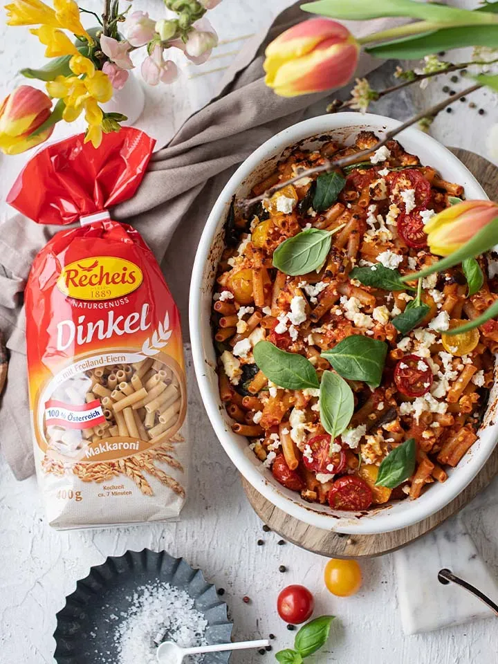 Nudelauflauf aus gebackenen Dinkel-Makkaroni mit Tomaten und Käse neben einer Packung Dinkelnudeln