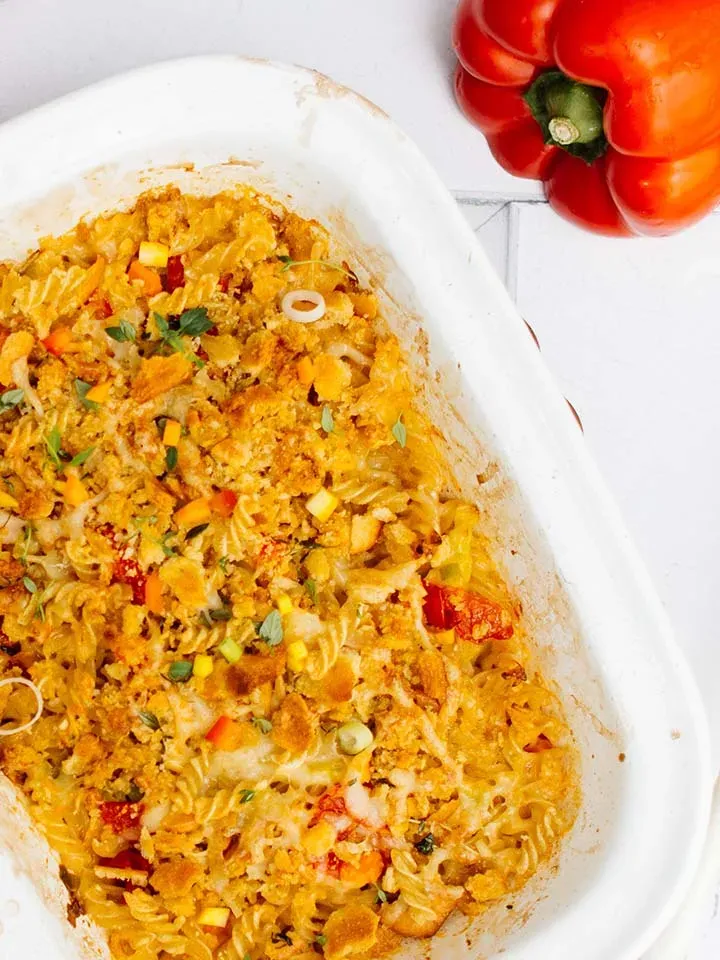 Nudelauflauf mit Gemüse und Käse in einer weißen Auflaufform neben roter Paprika