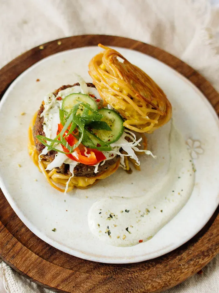 Nudelburger mit Spaghettibrötchen, Salat und Sauce auf einem weißen Teller